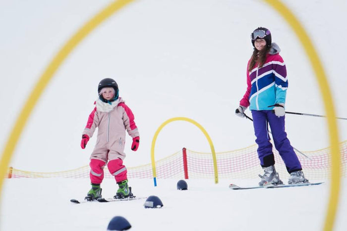 Skidlektion för barn: två barn på skidor med hjälm och skidjackor