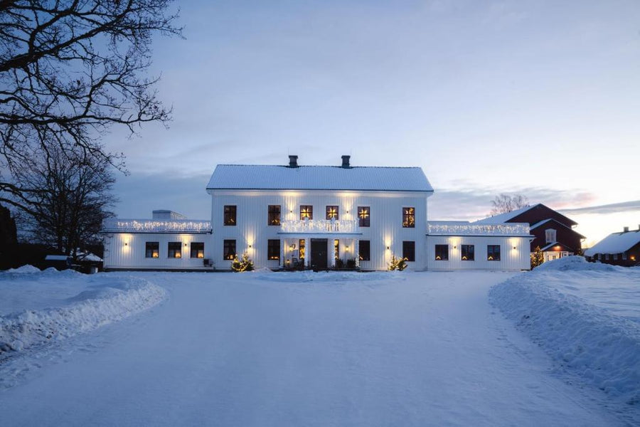 Vinterhus med upplysta fönster och sadeltak, sett framifrån i snö