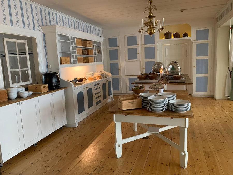 Frukost- och serveringsbord med porslin samt vitrinskåp i ljust kök
